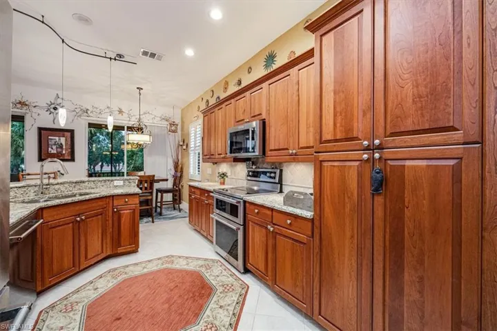 Kitchen featuring hanging light fixtures, light tile patterned floors, appliances with stainless steel finishes, light stone countertops, and sink