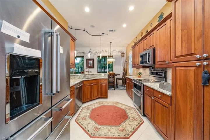 Kitchen featuring light stone countertops, light tile patterned flooring, appliances with stainless steel finishes, sink, and hanging light fixtures