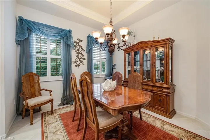Dining space with crown molding, a notable chandelier, a raised ceiling, and light tile patterned floors