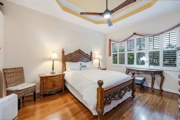 Bedroom featuring ornamental molding, a tray ceiling, wood-type flooring, and ceiling fan