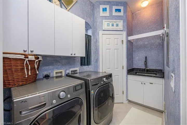 Laundry area featuring sink, light tile patterned flooring, washing machine and clothes dryer, and cabinets