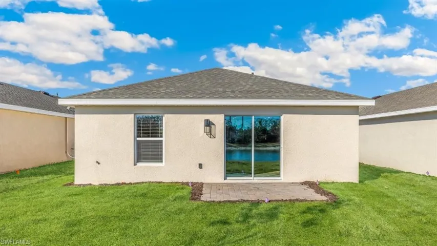 Model home. Back of house with a yard, stucco siding, a shingled roof, and a patio