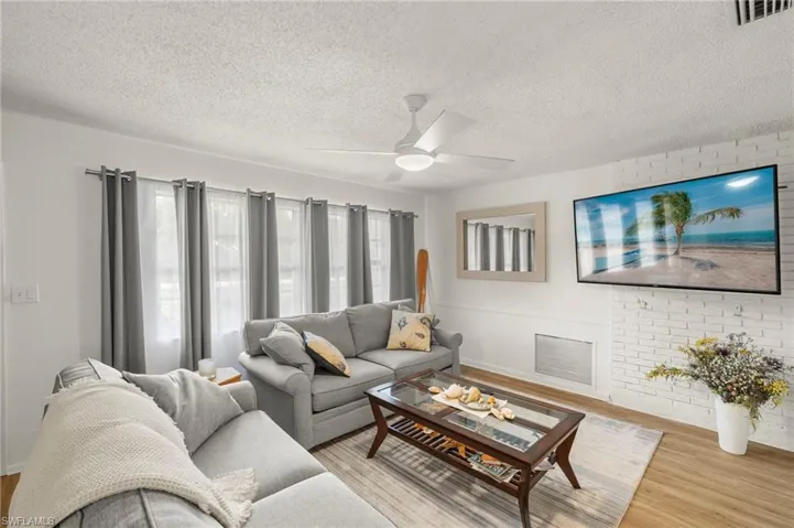 Living area with wood finished floors, a ceiling fan, a textured ceiling, and baseboards