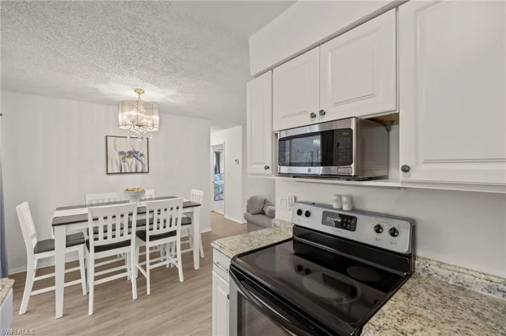 Kitchen with appliances with stainless steel finishes, a chandelier, light wood-type flooring, white cabinetry, and a textured ceiling