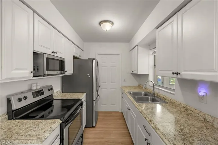 Kitchen featuring appliances with stainless steel finishes, a sink, white cabinetry, and light wood finished floors