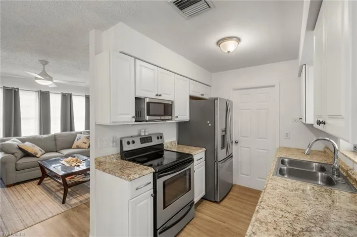 Kitchen with stainless steel appliances, a sink, open floor plan, a ceiling fan, and white cabinetry