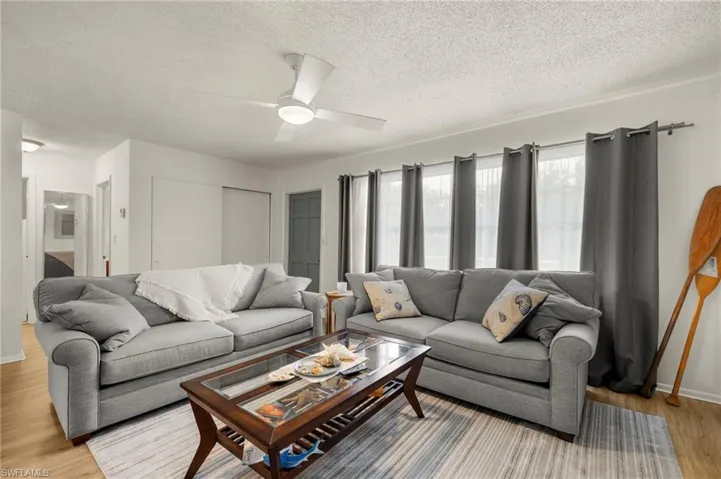 Living room with light wood-style flooring, a textured ceiling, ceiling fan, and baseboards