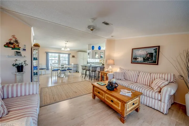Living area with a textured ceiling, light wood-style flooring, ornamental molding, and ceiling fan