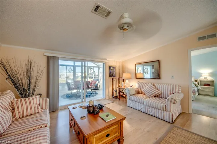 Living area featuring light wood-style floors, ornamental molding, a ceiling fan, and a textured ceiling