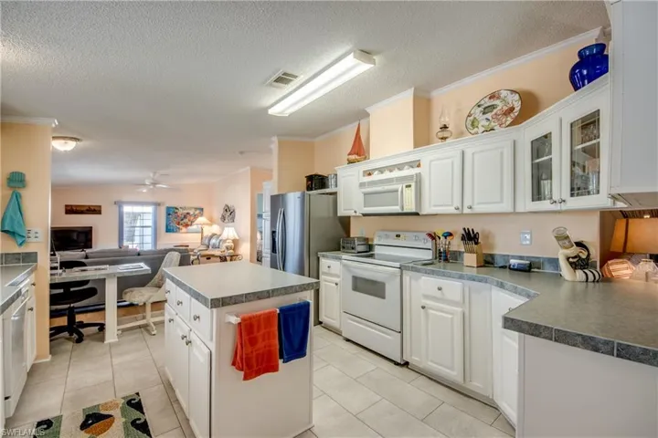 Kitchen with white appliances, open floor plan, white cabinets, crown molding, and a kitchen island