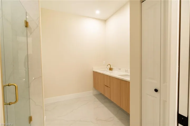 Bathroom featuring a floating double vanity with a light wood-finish, dual rectangular sinks, gold-finish faucets, and a marble-patterned countertop