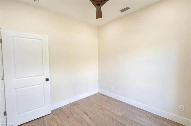 Room featuring wood-finish tile flooring, a white two-panel door with black hardware, neutral wall paint, and a wood-bladed ceiling fan