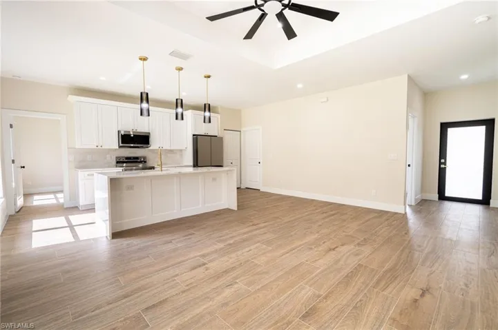 Open concept living area featuring wood-finish flooring, a contemporary kitchen island with pendant lighting, white shaker cabinetry, stainless steel appliances, and a tray ceiling with a black ceiling fan