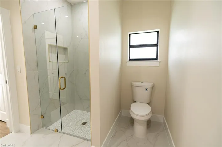 Glass-enclosed shower with gold-tone hardware, white marble-look tile, and a built-in shower niche