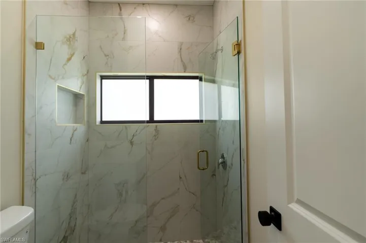 Glass-enclosed shower featuring large format marble-look tile, a built-in shower niche, and gold-finish hardware