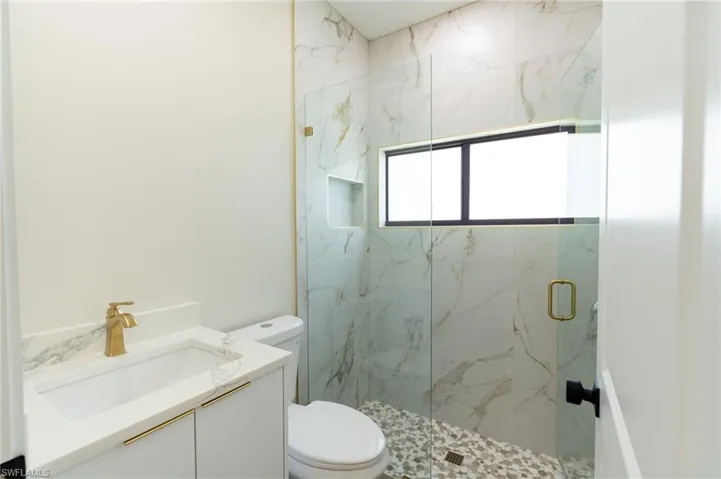 Contemporary bathroom featuring a frameless glass shower enclosure with gold-tone hardware, marble-finish wall tiling, and a mosaic pebble floor