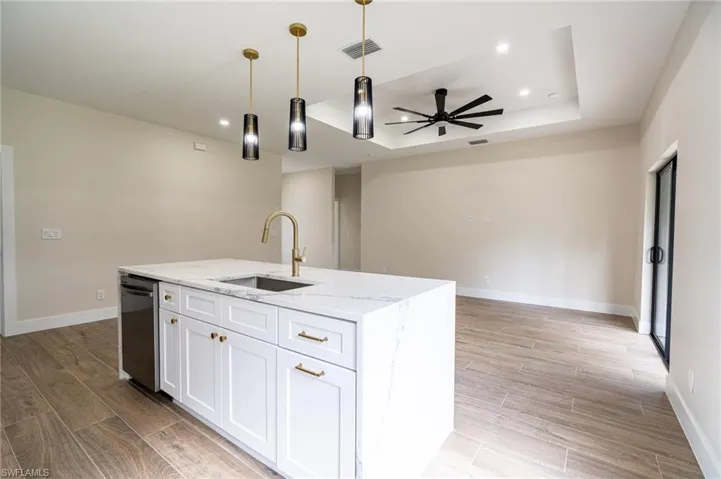 Kitchen island featuring white shaker cabinetry, gold-tone hardware, a stainless steel sink, and a gold-tone faucet