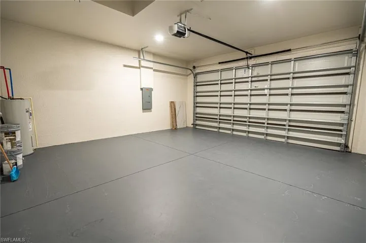 Spacious garage featuring a grey-painted concrete floor, textured cream walls, an overhead garage door opener, an electrical panel, and a water heater