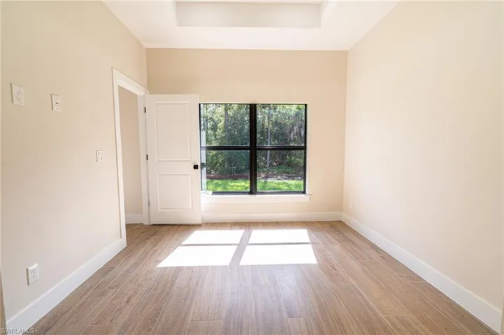 Room featuring wood-finish flooring, a tray ceiling, and a large window with black framing overlooking exterior greenery