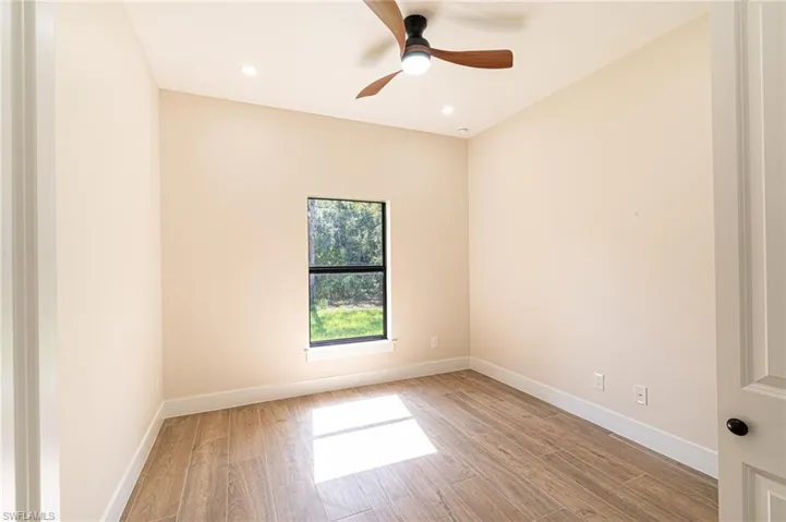 Room featuring wood-look tile flooring, a window with black trim, and a ceiling fan with integrated lighting