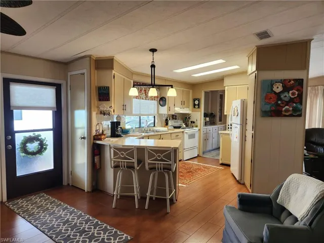 Kitchen featuring wood-type flooring, white appliances, kitchen peninsula, and hanging light fixtures