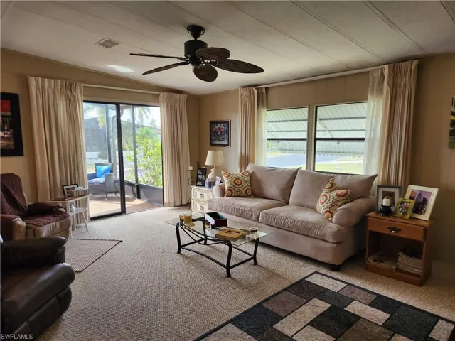 Carpeted living room with ceiling fan and vaulted ceiling