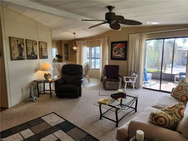 Carpeted living room with vaulted ceiling with beams, wood walls, and ceiling fan with notable chandelier