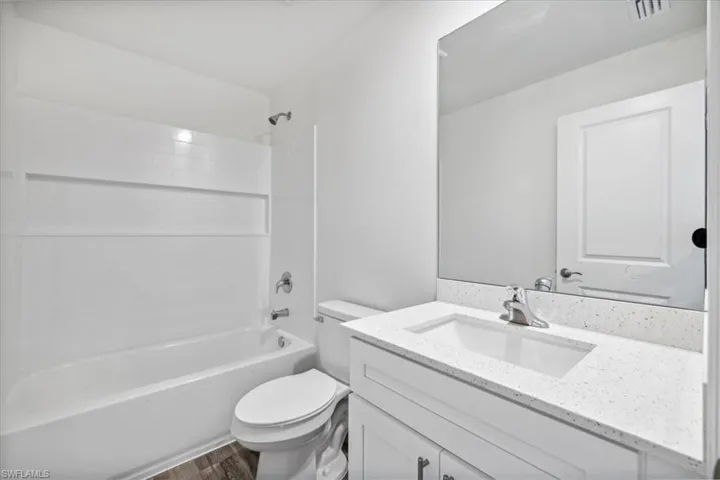 Full bathroom with hardwood / wood-style flooring, washtub / shower combination, vanity, and toilet