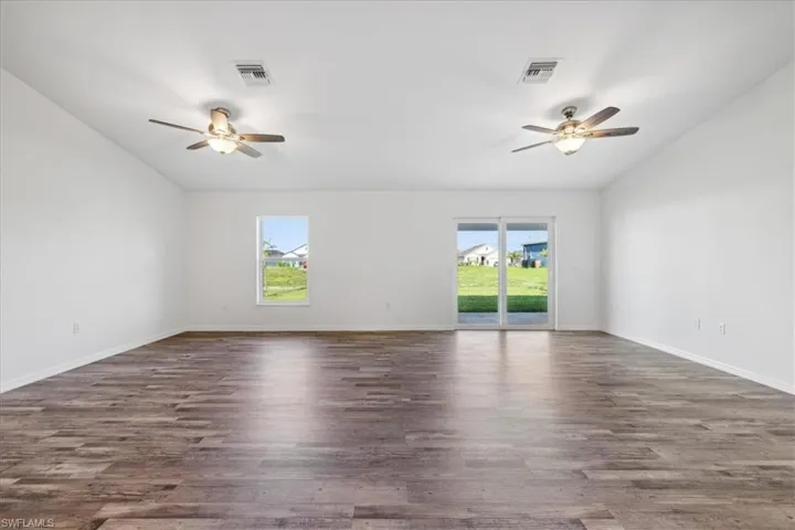 Unfurnished room featuring dark wood-type flooring, plenty of natural light, ceiling fan, and vaulted ceiling