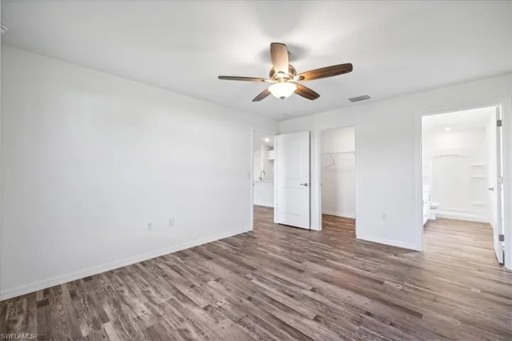 Unfurnished bedroom with connected bathroom, hardwood / wood-style floors, a spacious closet, a closet, and ceiling fan