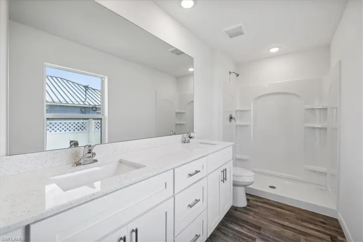 Bathroom with a shower, dual vanity, toilet, and hardwood / wood-style floors