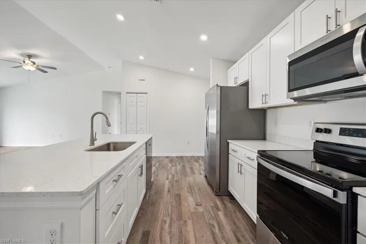 Kitchen featuring lofted ceiling, dark wood-type flooring, stainless steel appliances, sink, and ceiling fan