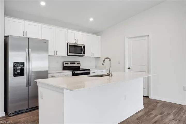 Kitchen with a center island with sink, wood-type flooring, sink, white cabinets, and appliances with stainless steel finishes