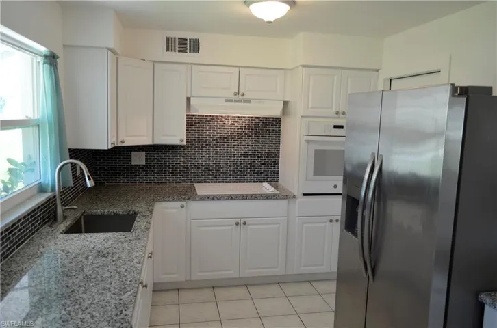 Kitchen with stainless steel fridge, light stone counters, white oven, white cabinets, and plenty of natural light