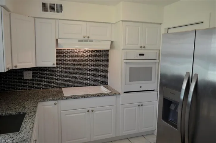 Kitchen with stainless steel fridge, white oven, white cabinetry, and light stone countertops