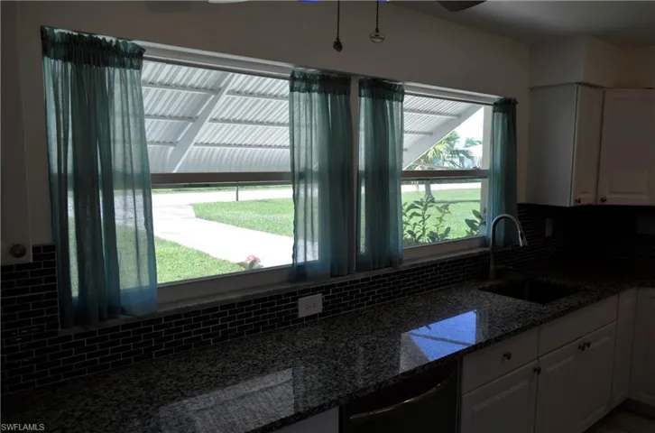 Kitchen featuring white cabinetry, light stone countertops, dishwasher, and backsplash
