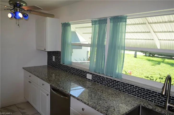 Kitchen with white cabinetry, tasteful backsplash, dark stone countertops, dishwasher, and a ceiling fan
