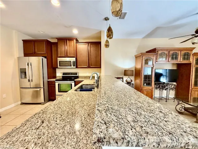 Kitchen featuring light tile floors, a ceiling fan, granite countertops, wooden cabinetry, and stainless steel appliances.