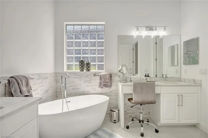 Bathroom with vanity, a soaking tub, a wainscoted wall, light tile patterned flooring, and tile walls