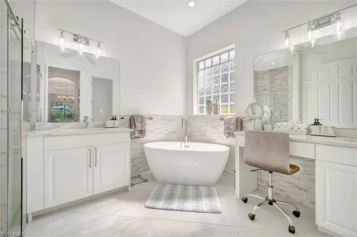 Full bathroom with two vanities, a stall shower, healthy amount of natural light, a freestanding tub, and tile walls