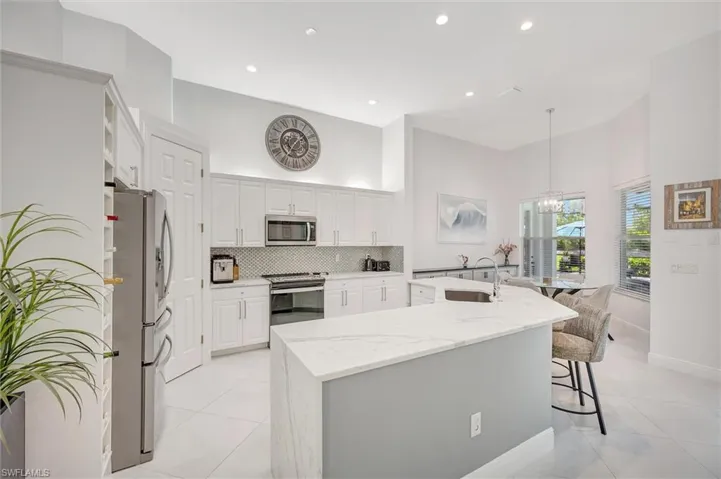 Kitchen with a large island with sink, light stone countertops, appliances with stainless steel finishes, a towering ceiling, and light tile patterned flooring