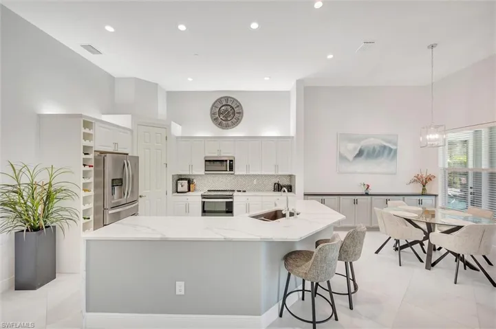 Kitchen featuring light stone counters, stainless steel appliances, backsplash, a spacious island, and white cabinetry
