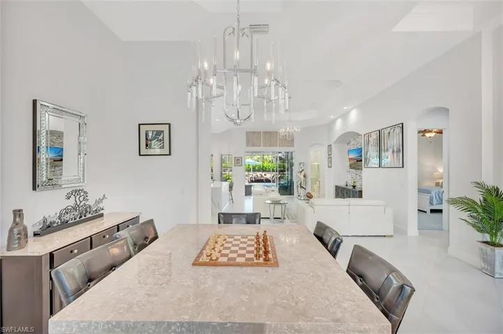 Dining area featuring arched walkways, a raised ceiling, a towering ceiling, ceiling fan, and a chandelier