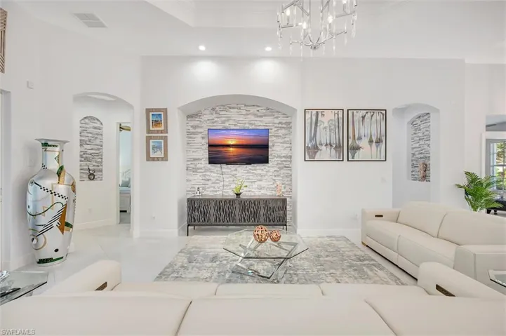 Living area with a raised ceiling, arched walkways, a chandelier, and ornamental molding