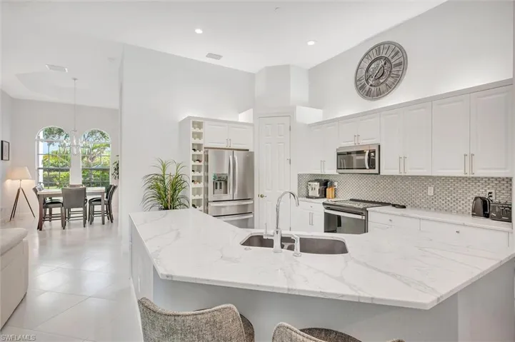 Kitchen with appliances with stainless steel finishes, light stone counters, decorative backsplash, pendant lighting, and white cabinets