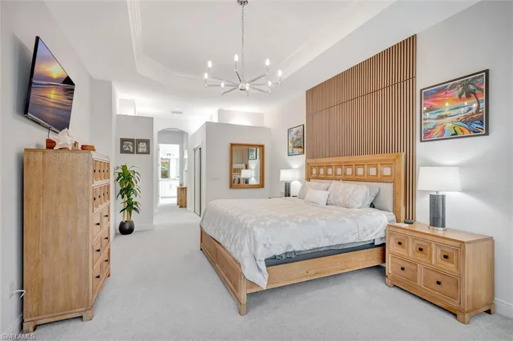 Bedroom featuring crown molding, light colored carpet, arched walkways, ensuite bathroom, and a tray ceiling
