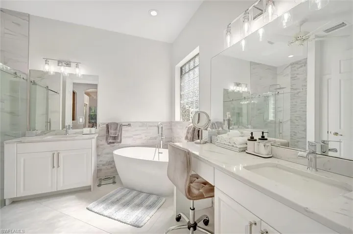 Full bath with two vanities, a marble finish shower, tile walls, a freestanding tub, and wainscoting