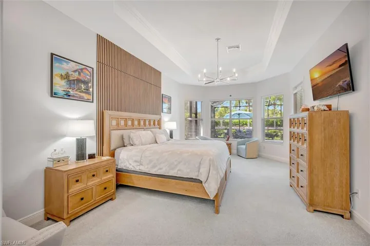 Bedroom with a tray ceiling, light colored carpet, a chandelier, and crown molding