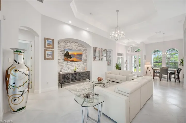 Living area with a raised ceiling, arched walkways, a chandelier, and ornamental molding
