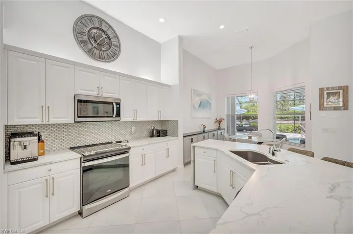 Kitchen with stainless steel appliances, light stone counters, white cabinetry, a high ceiling, and decorative light fixtures